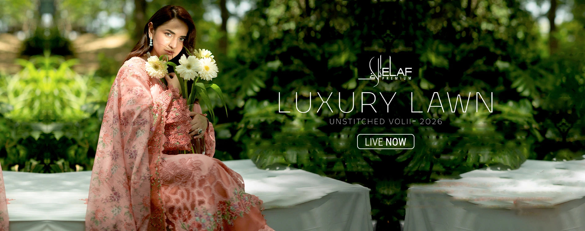 Wide homepage slider banner announcing the launch of Elaf Premium Luxury Lawn Unstitched 2026 Volume II collection, featuring a model holding white flowers outdoors while wearing a luxury peach pink unstitched three-piece embroidered lawn suit with a matching floral print dupatta.