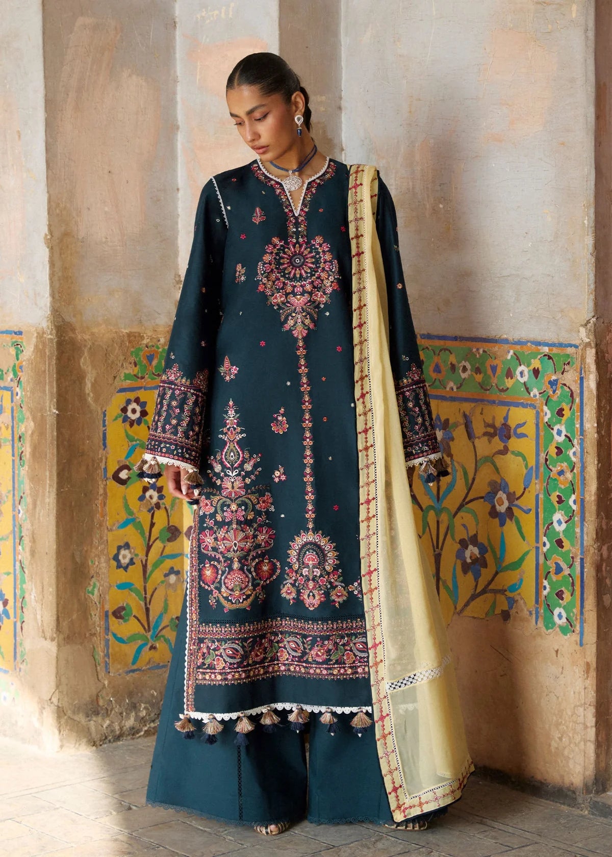 Studio portrait view highlighting the straight-line fall of the embroidered panels and contrasting mosaic wall background.
