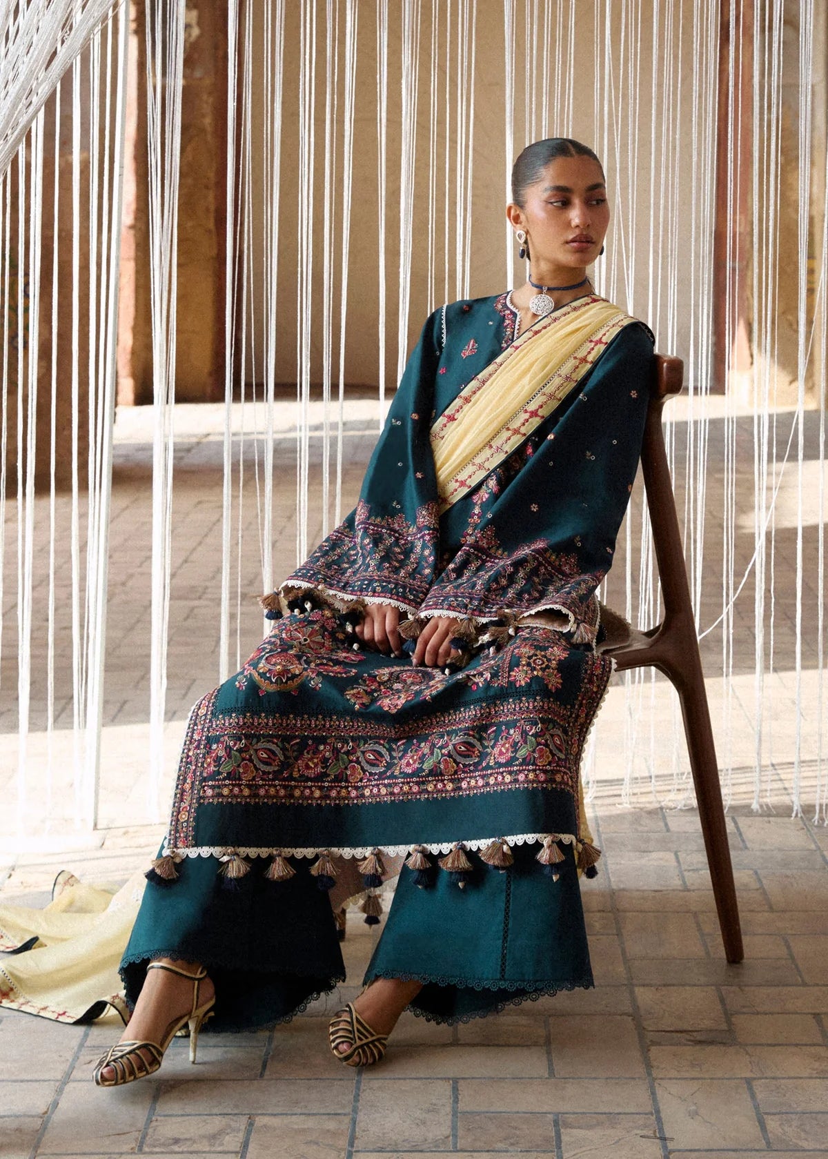 Full sitting presentation on a chair showcasing the heavy asymmetric panel embroidery, daman border design, and yellow dupatta.