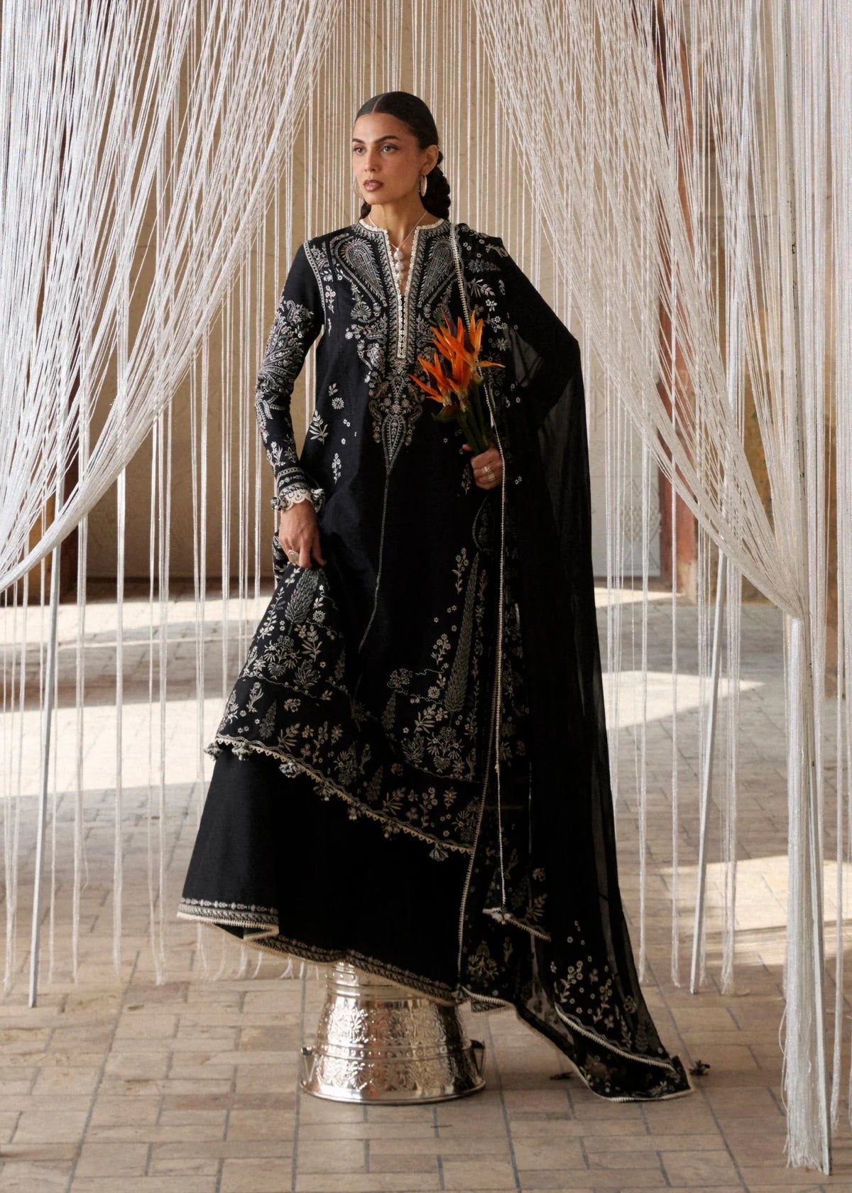 High-resolution close-up portrait focusing on the crisp white geometric and floral neckline embroidery details and sleeve borders on black fabric.