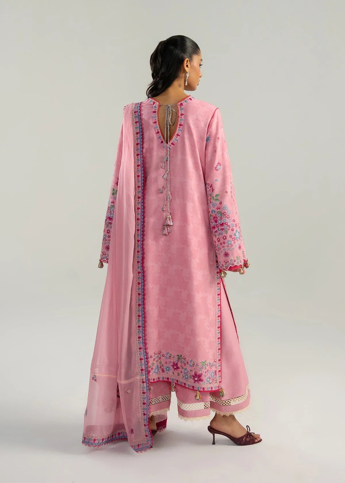 Rear model view showcasing the structural back panels, keyhole tassel ties, and delicate pink embroidery parameters on the hemline.